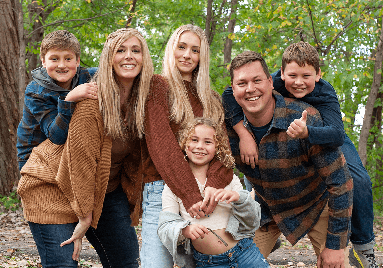 Family posing together in a wooded area.