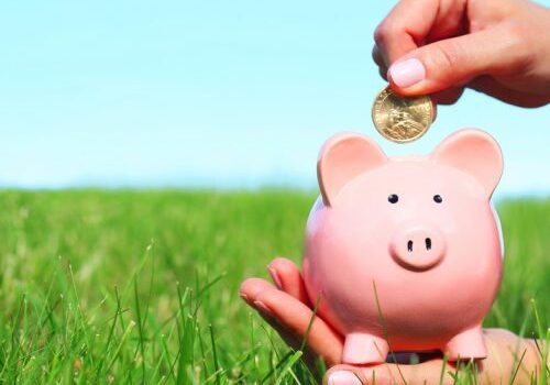 Hand placing coin in pink piggy bank