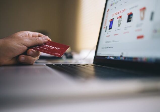 Hand holding credit card near laptop
